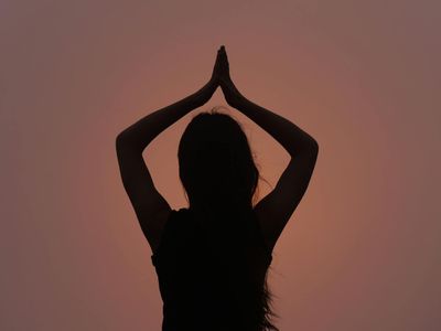 Silhouetted person in a yoga pose against violet light